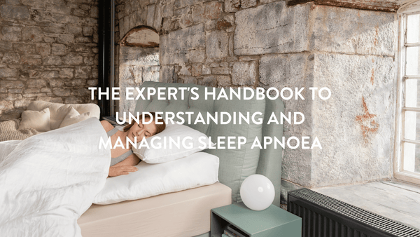 person lying on her side in bed with white bed linen and stone walls in the background 