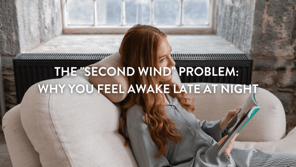 A woman with long red hair relaxing on a light couch, reading a book in a cosy room. 