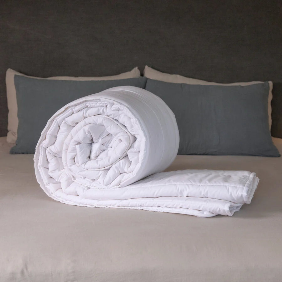 British Wool Summer Duvet 100% cotton handmade in the UK made to be hypo-allergenic, anti dust mite & sustainable. Rolled on a bed with visible cotton cover and Putnams tag, in a calm bedroom setting